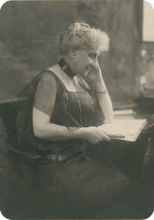 Ghenia Avril de Sainte-Croix sitting and reading at a desk