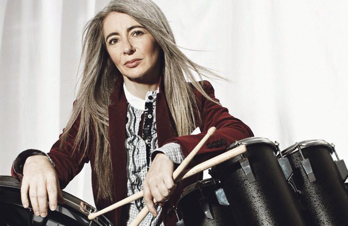 Evelyn Glennie next to drums and holding drumsticks